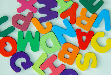 Fototapeta premium Multicolored plastic alphabet letters and a question mark symbol on a light green background, flat lay top view even layer composition, childhood education learning imagination creativity concept