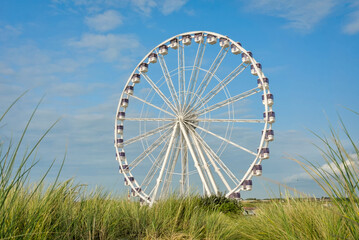 Big white Ferris wheel against a blue sky, seen from behind green grass, in Nieuwpoort-Bad.