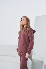 A woman stands in a casual burgundy hoodie and matching joggers, with her long hair cascading over...