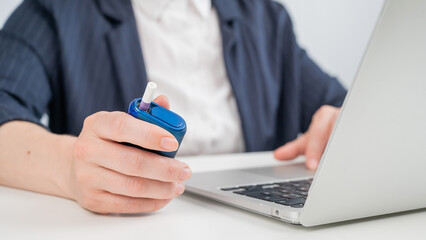 Business woman smoking an electronic cigarette while working on a laptop. Tobacco heating system.