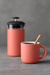 Preparing fresh coffee with a coral mug and stylish French press on gray surface