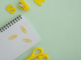 Notebook, paper clips, scissors and stapler on a light green background, top view. Space for text
