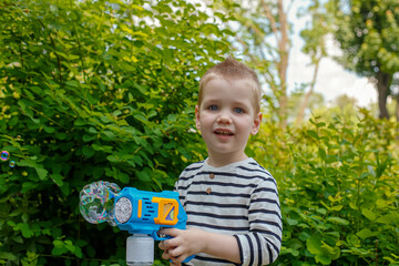 A smiling child plays with a bubble gun in a nature park.