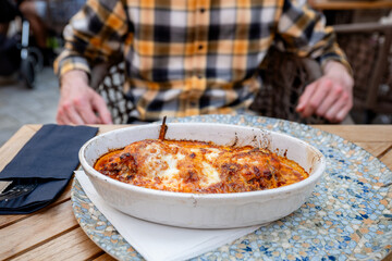 Baked pasta Bolognese with melted cheese in ceramic dish on restaurant table