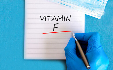 Vitamin F symbol. Concept words Vitamin F on beautiful white note. Doctor's hand in blue medical...