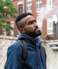 Young handsome African American man smoking cigarette in alley. Lips blowing smoke on blurred background. Portrait gangster smokes marijuana or cannabis. Portrait of a black guy smoking a cigarette.