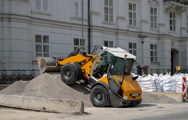 Yellow loader on gravel pile at construction site in front of white building