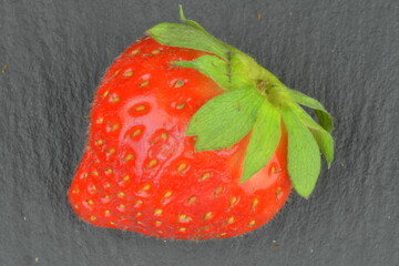 Macro shot of a ripe red strawberry on a black backdrop. Ripe strawberry on a black stone backdrop. Close-up and view from above