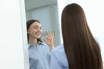 Fototapeta premium Beautiful woman showing ok gesture near mirror indoors
