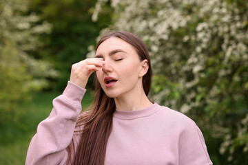 Woman suffering from seasonal pollen allergy near blossoming shrub on spring day