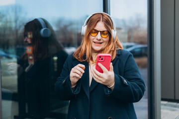 30s millennial Caucasian lady student in wireless headphones with phone listen music, enjoy audio...