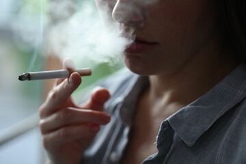 Woman smoking cigarette indoors, closeup. Bad habit