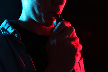 Man using electronic smoking device in neon lights on black background, closeup