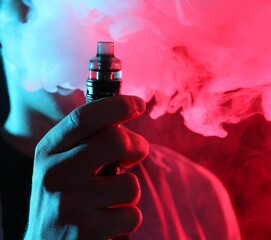 Man using electronic smoking device in neon lights on dark background, closeup