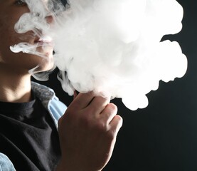 Man using electronic smoking device on black background, closeup