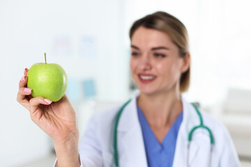 Nutritionist with green apple and stethoscope in clinic, selective focus
