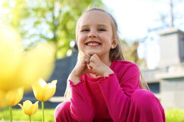 Cute little girl near beautiful yellow tulips outdoors