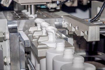 Molding of white plastic bottles. Automated production line for casting white plastic bottles. White plastic bottles on a production line. Liquid packaging