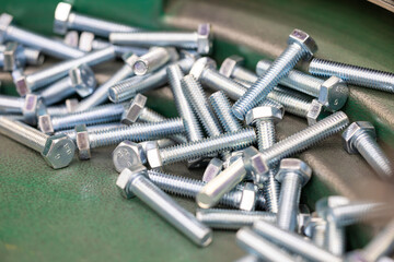 Threaded Steel Bolts on Vibratory Feeder in Manufacturing Plant. Detailed image of threaded bolts moving along a green vibratory feeder in an automated production line. Selected focus