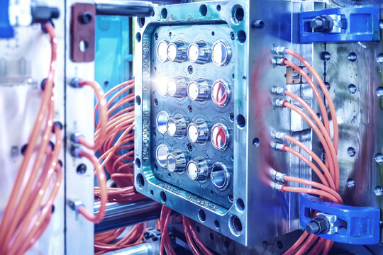 Close-up of an industrial plastic injection molding machine with bright orange cables attached to metallic components. High-tech manufacturing concept