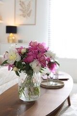 Bouquet of beautiful peonies and water on coffee table indoors. Interior design