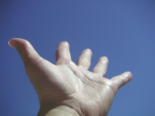 An outstretched hand reaching towards a clear blue sky on a bright day