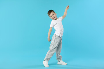 Happy little boy dancing on light blue background. Space for text