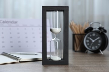 Deadline. Hourglass with flowing sand, stationery, calendar and alarm clock on wooden table indoors