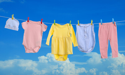 Different baby clothes drying on washing line against blue sky