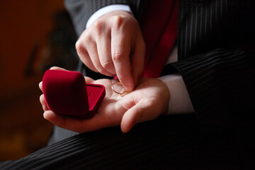 Man proposing with a gold wedding ring in a red velvet box
