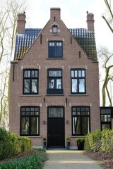 Naklejka premium Modern brick house with black trim surrounded by greenery in a tranquil setting, featuring large windows and a pitched roof in the early afternoon light