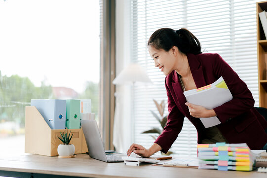 Female employee working with pile of documents to search for information and check documents on desk in office. Accounting income, expenses, tax records and hard work.