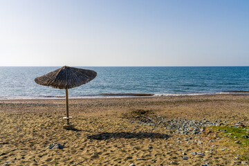 Single straw umbrella standing on quiet beach at sunset. Peaceful seaside atmosphere with warm...
