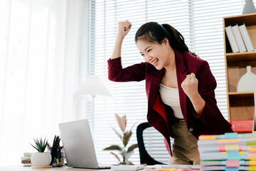 Asian woman is excited about her victory in the office. Female employees are very happy about their...