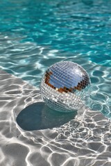 Shimme disco ball floating on water surface with ripples in the sunlight creating reflections and shadows du daytime