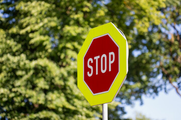 bright red and yellow stop sign against green tree background traffic warning road sign outdoor...