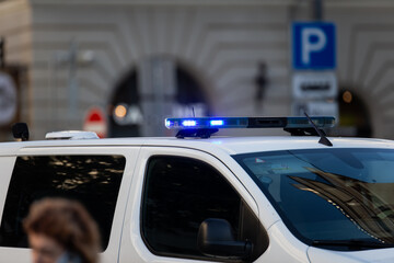 white police van with flashing blue sirens parked in european city center street urban law...