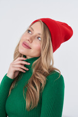 Smiling person wearing a vibrant red hat and a green sweater, gazing upward with long blond hair....