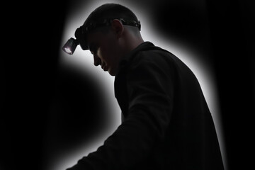 A silhouette of a man wearing a headlamp, symbolizing a miner or worker embarking on dangerous work or travel through a dark mine. This image captures the essence of a dedicated team © tanitost