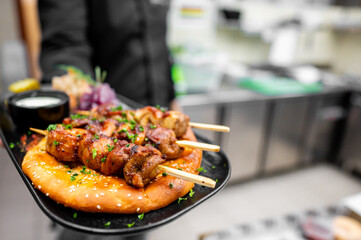 Close-up of grilled meat skewers with herbs on a sesame bun, served with sauce and pickled...