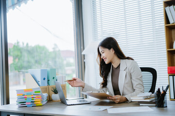 Confident Businesswoman at Work: A smiling young businesswoman confidently works at her desk,...