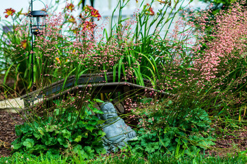 Buddha statue in flower garden with wooden bridge on sunny day