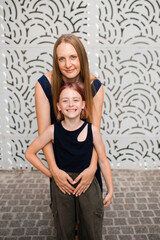 Smiling woman holding id girl together outdoors over gray wall. Looking at camera. Motherhood.