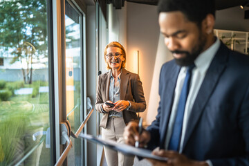 businesswoman use cellphone at workplace while black man stand in front
