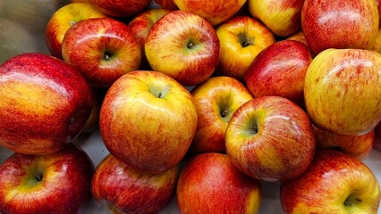 displays a pile of fresh apples. They are predominantly red with significant yellow patches, indicating a variety like Gala or Fuji apples. The apples are stacked in a way that suggests they are ready