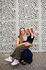 Happy mother having fun with child girl daughter in city street over gray wall. Motherhood.