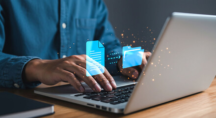 A person typing on a laptop with file transfer icons floating above the keyboard on a wooden desk