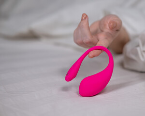 Woman holding curved pink vibrator while lying in bed. 