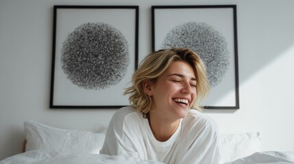 Woman with short blonde hair, laughing joyfully in bed in a brightly lit, minimalist bedroom with modern art