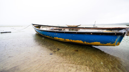 Fishing boat anchored on the sand of a dry beach. Quite rainy day with dense clouds.